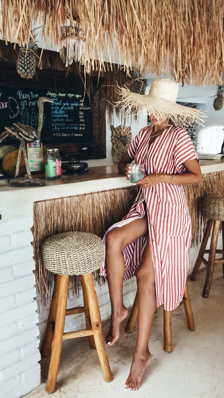 Boho chic woman wearing a straw hat sitting in a bar in Saint-Tropez