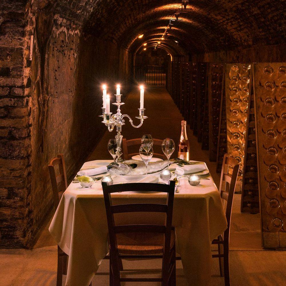 Table with candles and bottle of Crystal vintage 2008 champagne in wine cellar.