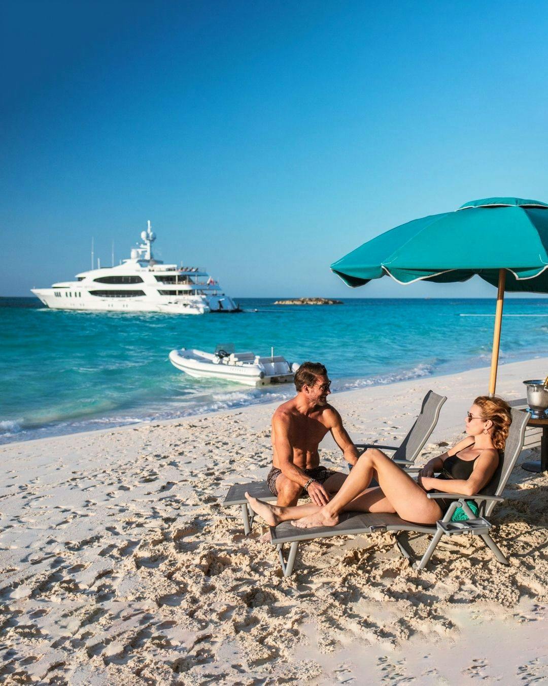 Man and woman sunbathing on a beach under umbrella.