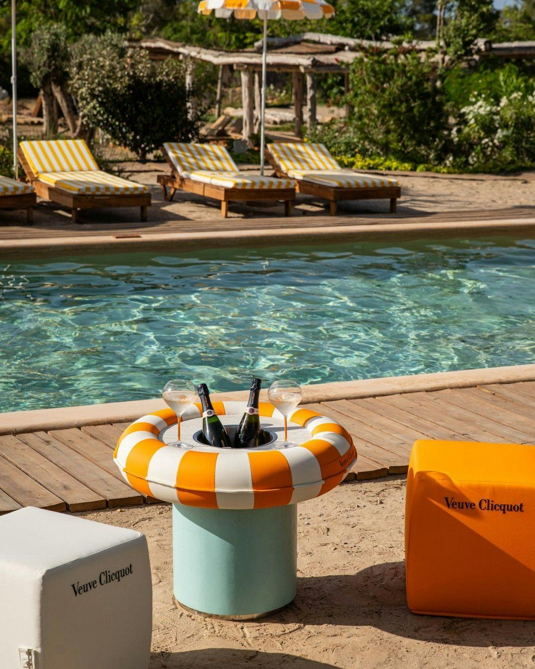 Two bottles of Veuve Clicquot in a cooler next to a swimming pool.