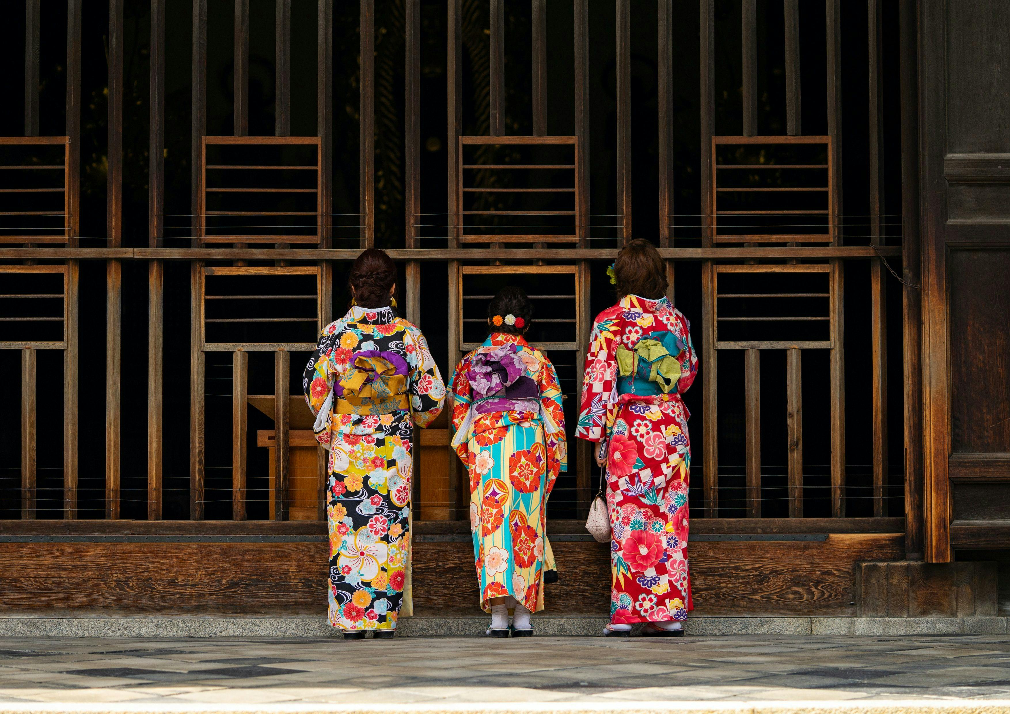 Three geishas standing next to a wooden wall