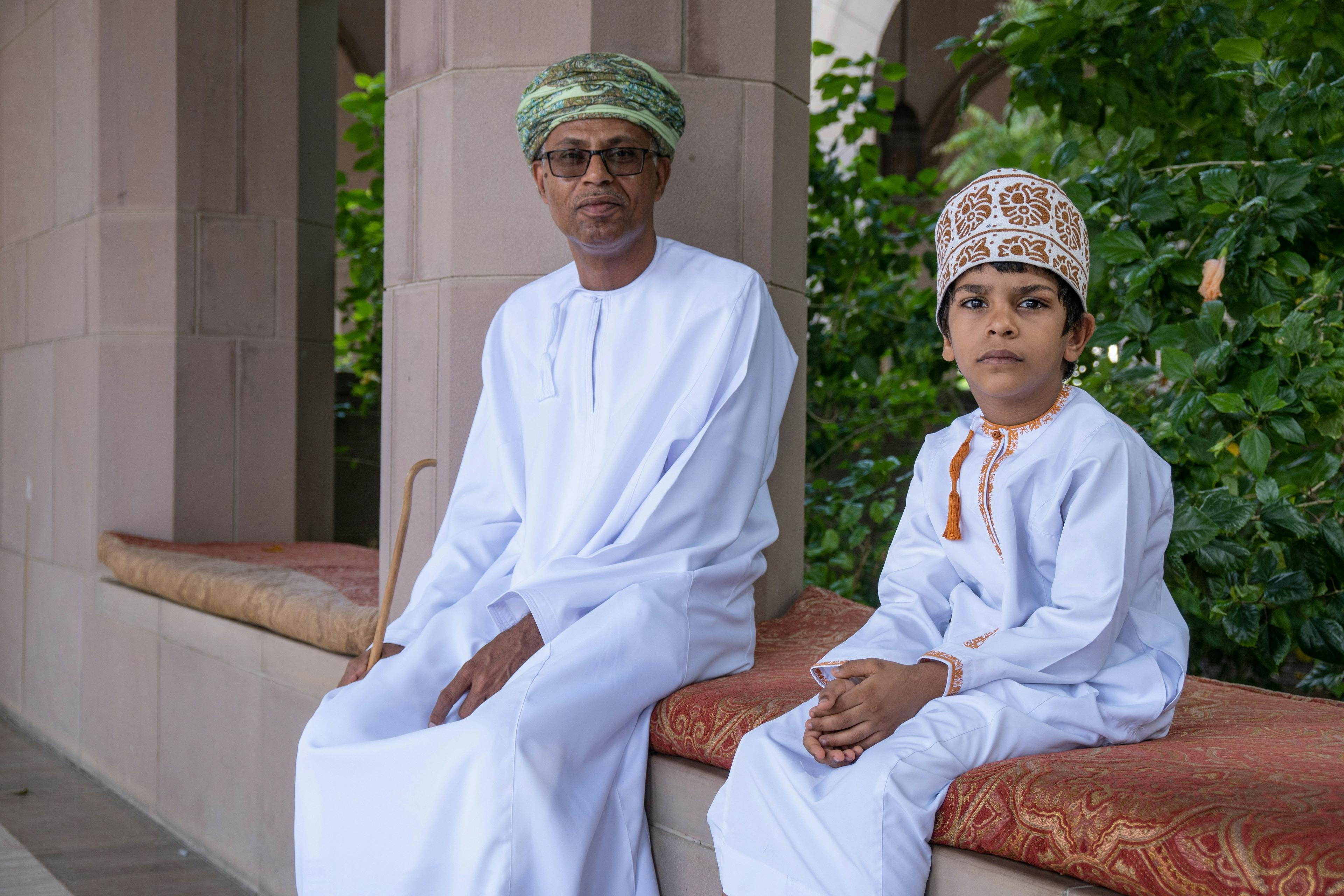 Local boy and man sitting next to a mosque in Oman.