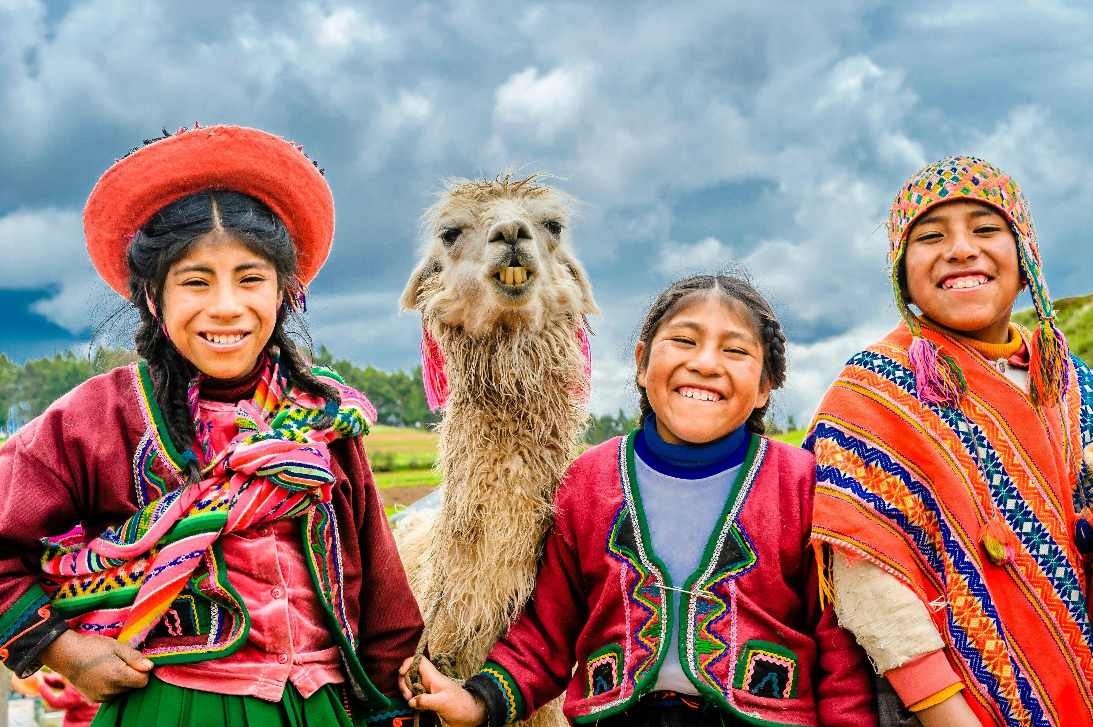 Local children in traditional clothing smiling in camera in Peru.