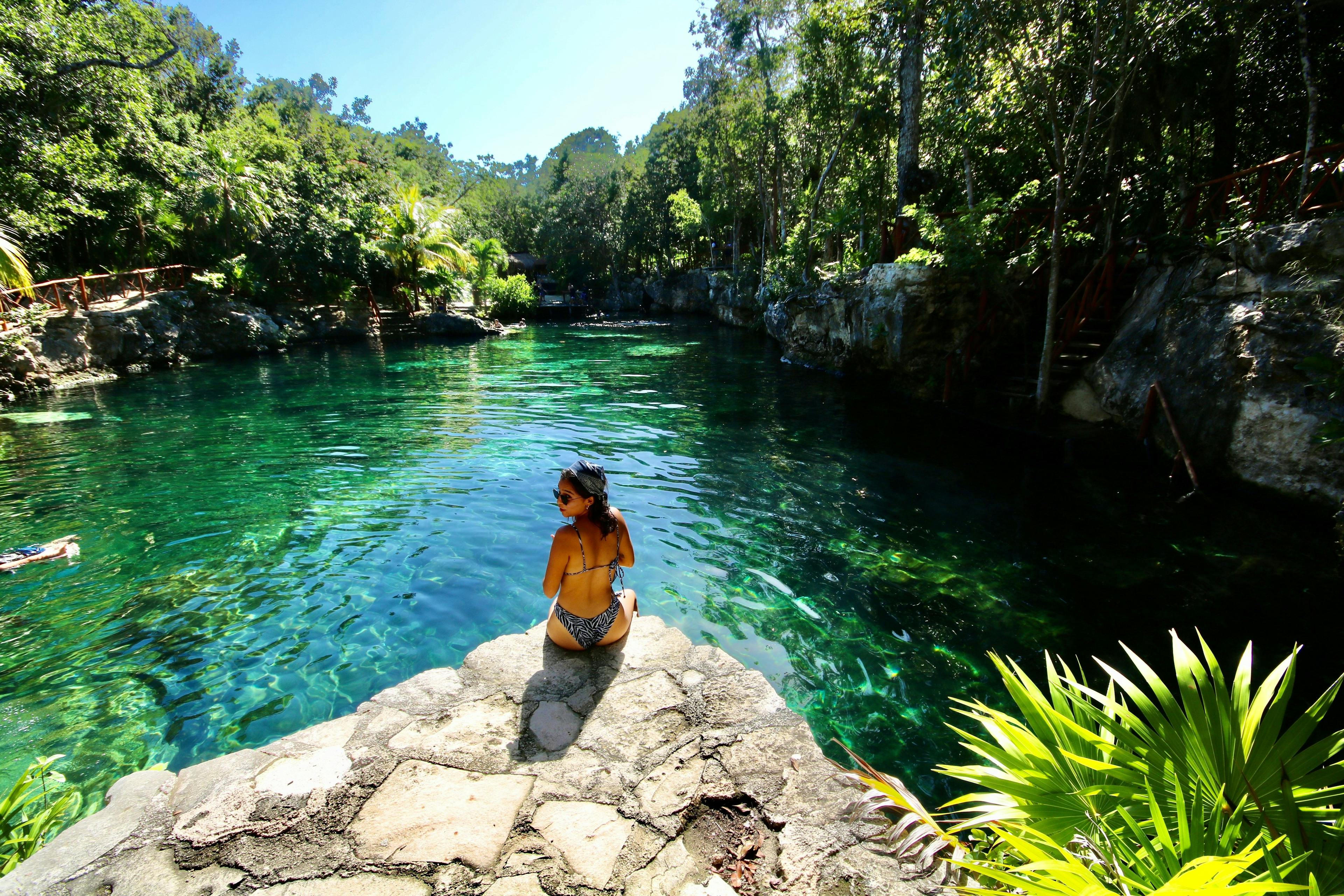 Woman sitting near cenote with crystal clear water in Tulum Mexico